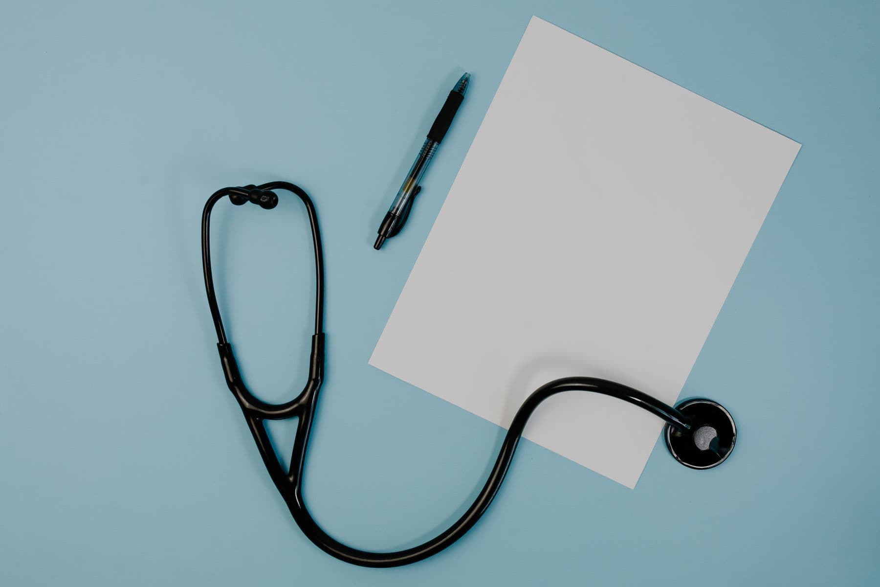 A stethoscope, a pen and a blank sheet of paper on a blue surface