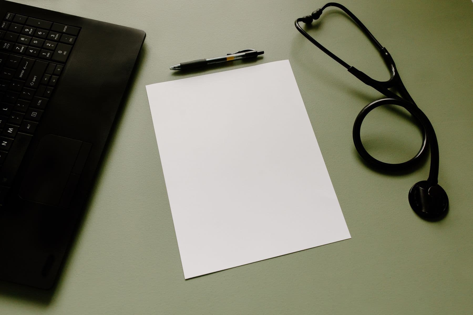 A stethoscope, a pen and a sheet of paper beside a laptop